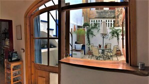 Habitació amb finestra de fusta corbada que dona a un petit pati exterior amb taula i cadires.