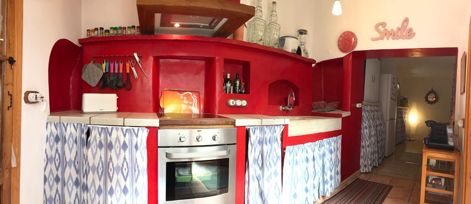 Une cuisine compacte avec un mur d’accent rouge, un four encastré et une variété d’ustensiles de cuisine.