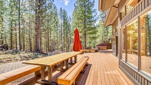 A wooden deck with picnic tables and benches, surrounded by tall pine trees. - Pools, Private Hot Tub & Pool Table. Upscale Lodge (Sisters)
