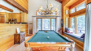 A pool table in a wooden cabin with a large window and a chandelier. - Pools, Private Hot Tub & Pool Table. Upscale Lodge (Sisters)