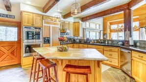 A spacious kitchen with wooden cabinets, a large island with stools, stainless steel appliances, and a bar sign. - Pools, Private Hot Tub & Pool Table. Upscale Lodge (Sisters)