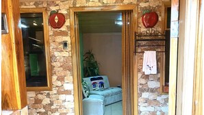 Käytävä, jonka seinät ovat kivestä, lattia laatoitettu ja oviaukko johtaa huoneeseen, jossa on sohva ja kasvi.