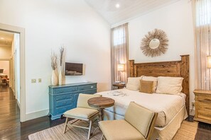 Ein Schlafzimmer mit einem großen Bett, einem Holz-Kopfteil, einer blauen Kommode, einem runden Tisch, zwei Stühlen und einem dekorativen Spiegel an der Wand.