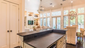 Una cocina amplia con una isla grande, un comedor con sillas de madera y una sala de estar con sofá y televisor.