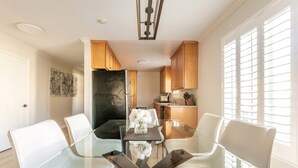 Una cocina moderna con armarios de madera, una isla central y un comedor con mesa de vidrio y sillas blancas.
