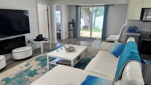 Een moderne woonkamer met een flatscreen televisie, witte meubels en uitzicht op het omliggende landschap.
