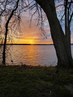 Un coucher de soleil sur un lac paisible, avec des arbres encadrant le paysage.