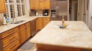 A kitchen with wooden cabinets, a stainless steel refrigerator, a marble countertop, and a pendant light. - Well-equipped 3BR/3BA with large common space in the heart of Historic Downtown (New Iberia)