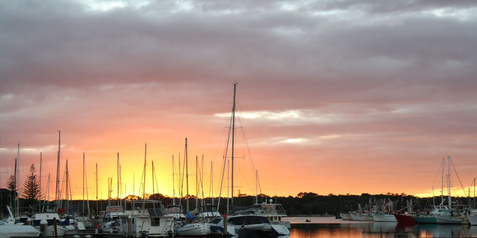 A marina with multiple boats docked under a sunset sky.