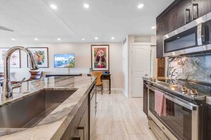A modern kitchen with a large island, stainless steel appliances, and artwork on the walls.