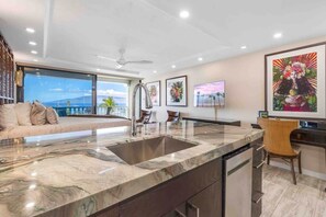 A modern kitchen with a large island, a dining area with a sofa, and a view of the ocean. - Lahaina Shores Ocean Front Luxury Condo 525 (Lahaina)