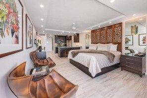 A modern hotel room with a large bed, a sitting area with a chair, a desk, and a kitchenette in the background. - Lahaina Shores Ocean Front Luxury Condo 525 (Lahaina)