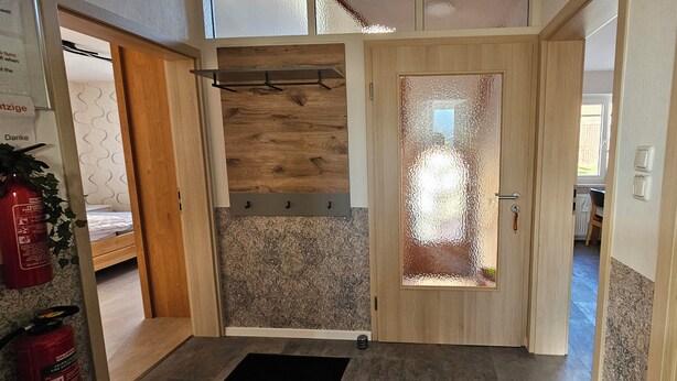 A room with a wooden door, a bed, and a small table with a plant. - Apartment Fulda 65m² up to 6 pers. (Fulda)