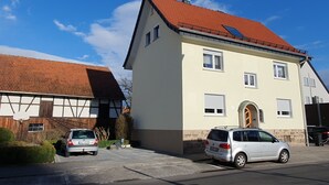 A two-story building with a red-tiled roof, a garage, and two parked cars. - Apartment Fulda 65m² up to 6 pers. (Fulda)