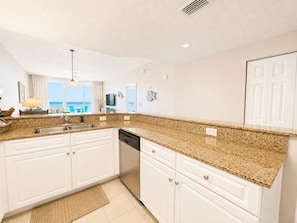 A modern kitchen with white cabinets, granite countertops, and a built-in dishwasher.