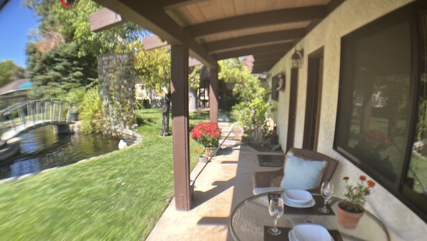 Une terrasse avec une table dressée pour deux personnes, un petit jardin et une vue sur une maison.