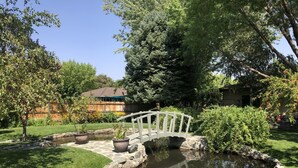 Un jardin avec un étang, un pont en bois et une maison en arrière-plan.