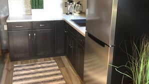 Une cuisine moderne avec des meubles en bois foncé, des appareils électroménagers en acier inoxydable, un tapis à rayures et une plante en pot.