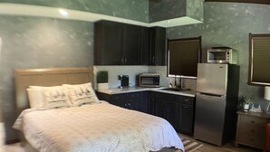 Une chambre avec un lit, un coin cuisine et un ventilateur de plafond.