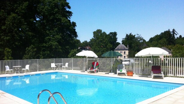 A rectangular swimming pool with a metal ladder, surrounded by a white fence. There are lounge chairs and umbrellas in the background.