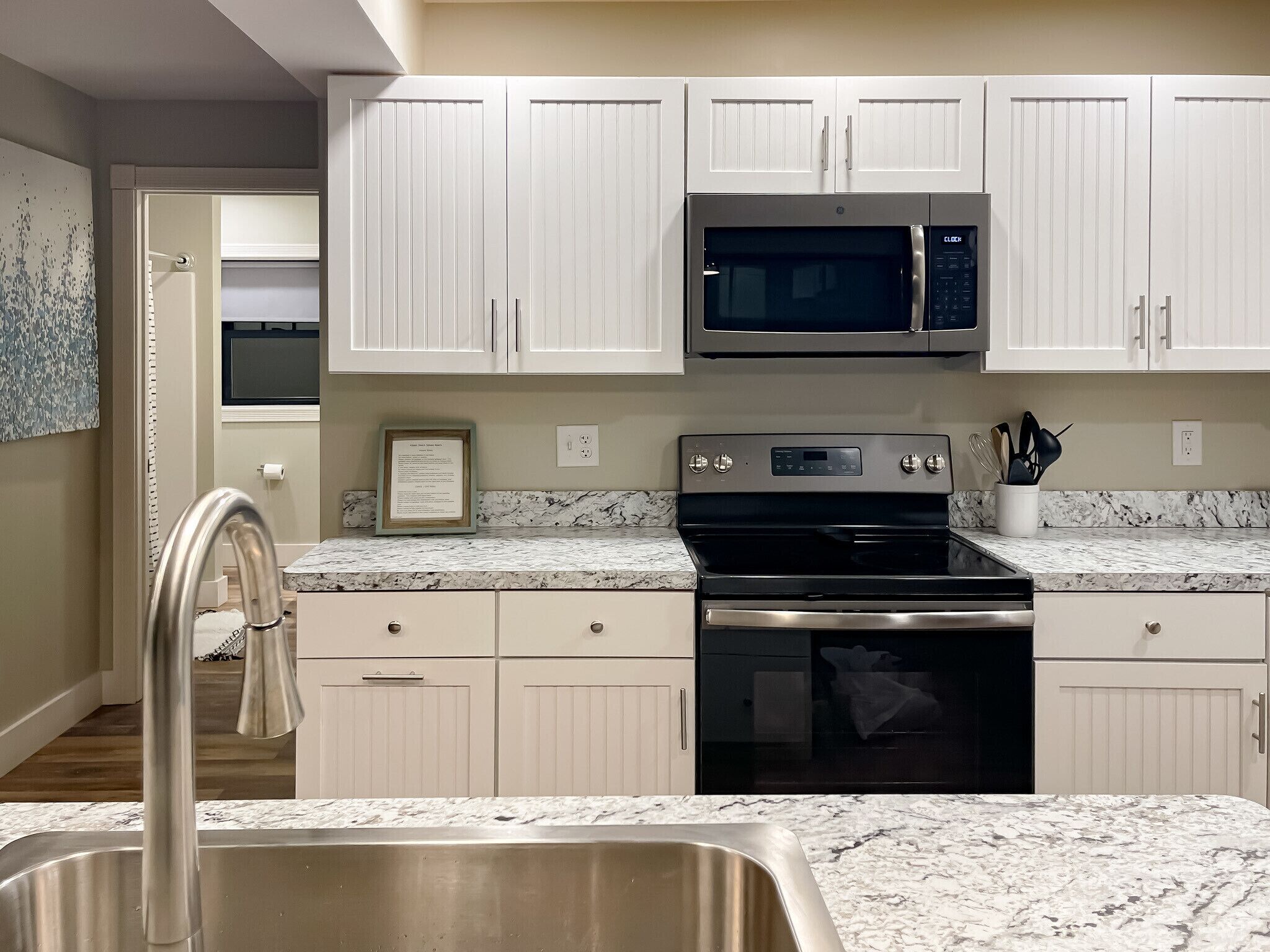 A modern kitchen with white cabinets, a stainless steel sink, a black stove, and a microwave.