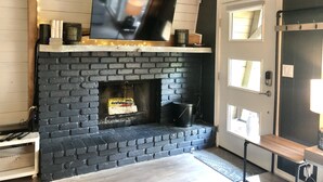 Een moderne woonkamer met een zwart metselwerk schoorsteen, een wandgemonteerde flatscreen televisie en een houten plafond met lichtjes.