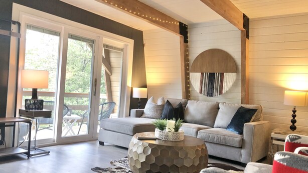 Een gezellige woonkamer met een bank, een ronde salontafel en een vloerkleed. Er is een groot raam met uitzicht op bomen.