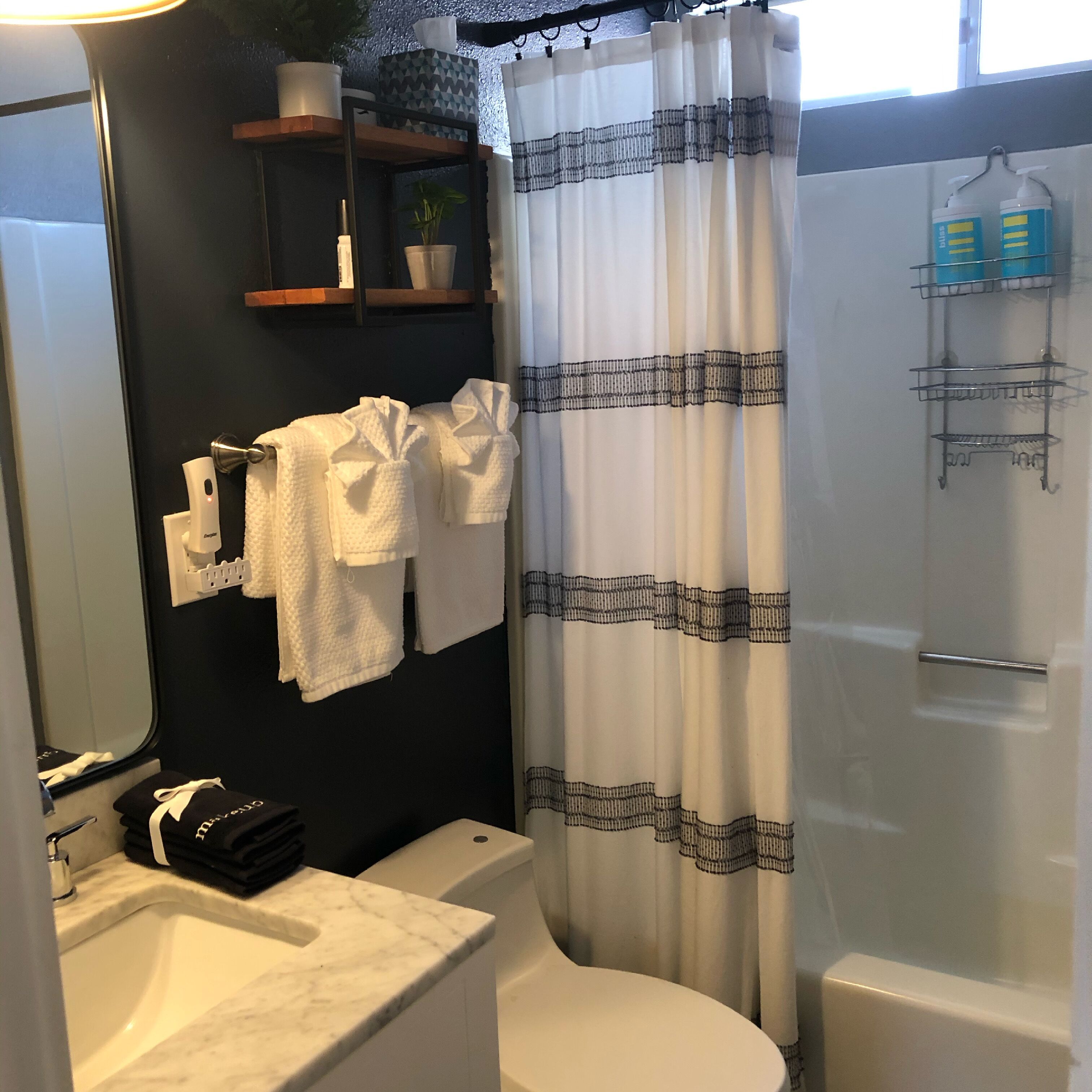A bathroom with a white bathtub, a white toilet, a sink with a marble countertop, a shower curtain, and a towel rack with folded towels.