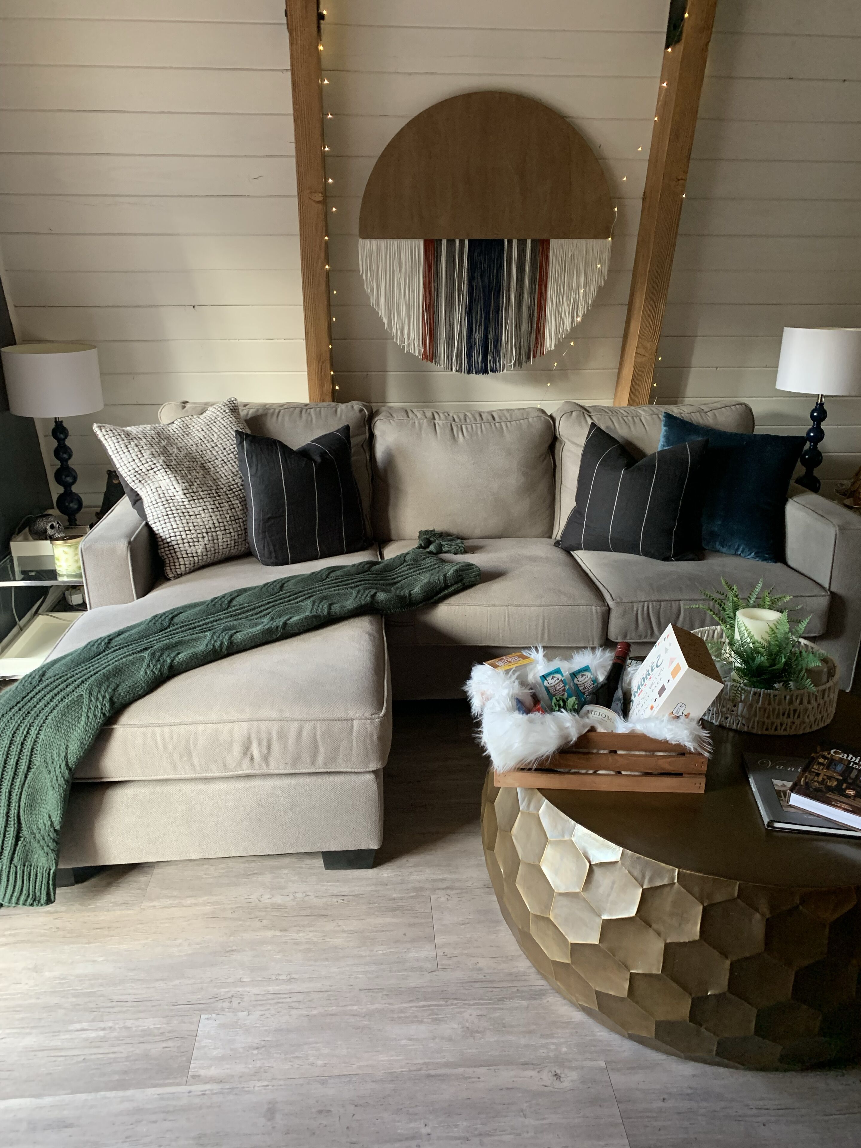 A cozy living room with a beige sectional sofa, a green throw blanket, and a decorative wall hanging.