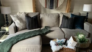 Een gezellige woonkamer met een beige hoekbank, een groene plaid en een decoratieve wandversiering.