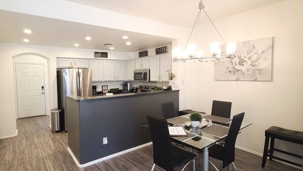 A modern kitchen with white cabinets, stainless steel appliances, and a central island. There is a dining area with a glass table and black chairs.