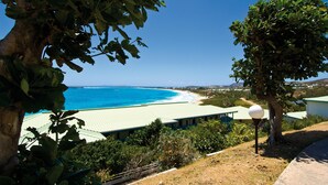 A coastal view with a building and a tree in the foreground. - Luxury studios with ocean view on Orient bay (Mont Vernon)