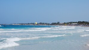 A beach with clear blue water, a sandy shore, and a distant view of a city skyline. - Luxury studios with ocean view on Orient bay (Mont Vernon)