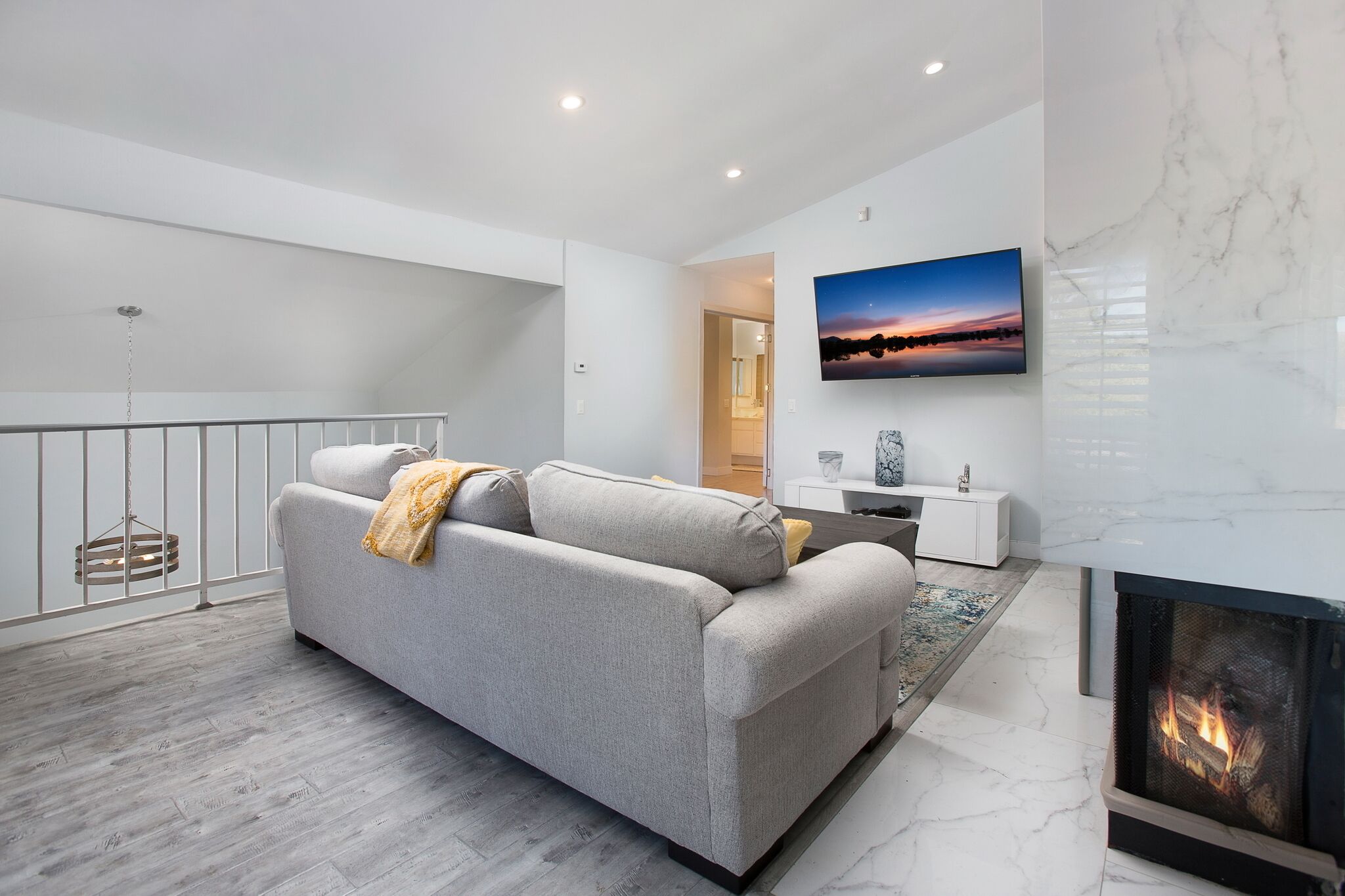 A modern living room with a grey sofa, a fireplace, a flat-screen TV, and a marble wall.