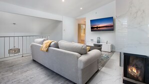 En moderne stue med en grå sofa, en pejs, et fladskærms-tv og en marmorvæg.