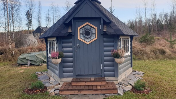 A log cabin with a dark gray exterior, a hexagonal window, and a wooden door. - Adeli Holiday Cottage Ellivuori with hot tube and grill hut (Ellivuori)