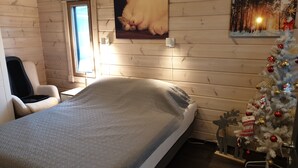 A cozy room with a bed, a chair, a Christmas tree, and a painting of a cat. - Adeli Holiday Cottage Ellivuori with hot tube and grill hut (Ellivuori)