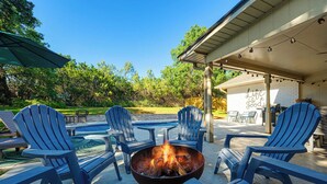Eine Terrasse im Freien mit Adirondack-Stühlen, einem Feuerkorb und einem Pool.