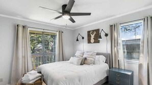 Ein Schlafzimmer mit einem Bett, Nachttischen, einem Deckenventilator und einem Fenster mit Vorhängen.