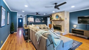 Ein modernes Wohnzimmer mit einem Ecksofa, einem Kamin, einem Fernseher und Deckenventilatoren.