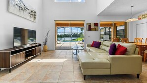 Uma sala de estar espaçosa com uma televisão grande, um sofá de couro e uma área de jantar com cadeiras de madeira.