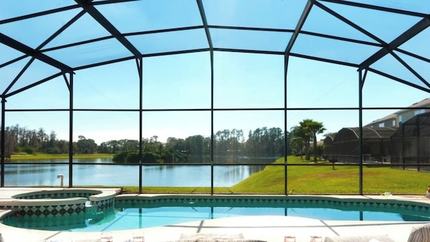 Uma área de piscina com vista para um lago, mobiliário de exterior e uma secção coberta.