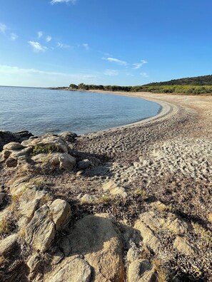 Ein Kiesstrand mit großen Steinen im Vordergrund und einem klaren, blauen Himmel.