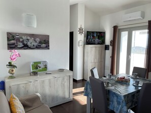 Un salon moderne avec un coin repas, comprenant un meuble en bois, un téléviseur et une grande fenêtre avec des rideaux.