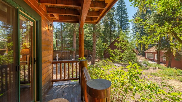 A wooden deck with a glass door leading to a room, surrounded by a forested area.