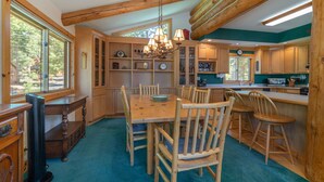 A spacious kitchen with wooden cabinets, a dining table, and chairs. There is a large window providing natural light and a view of the outdoors.
