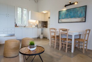 Et moderne køkken med hvide skabe, et spiseområde med træstole og et rundt bord med en plante.