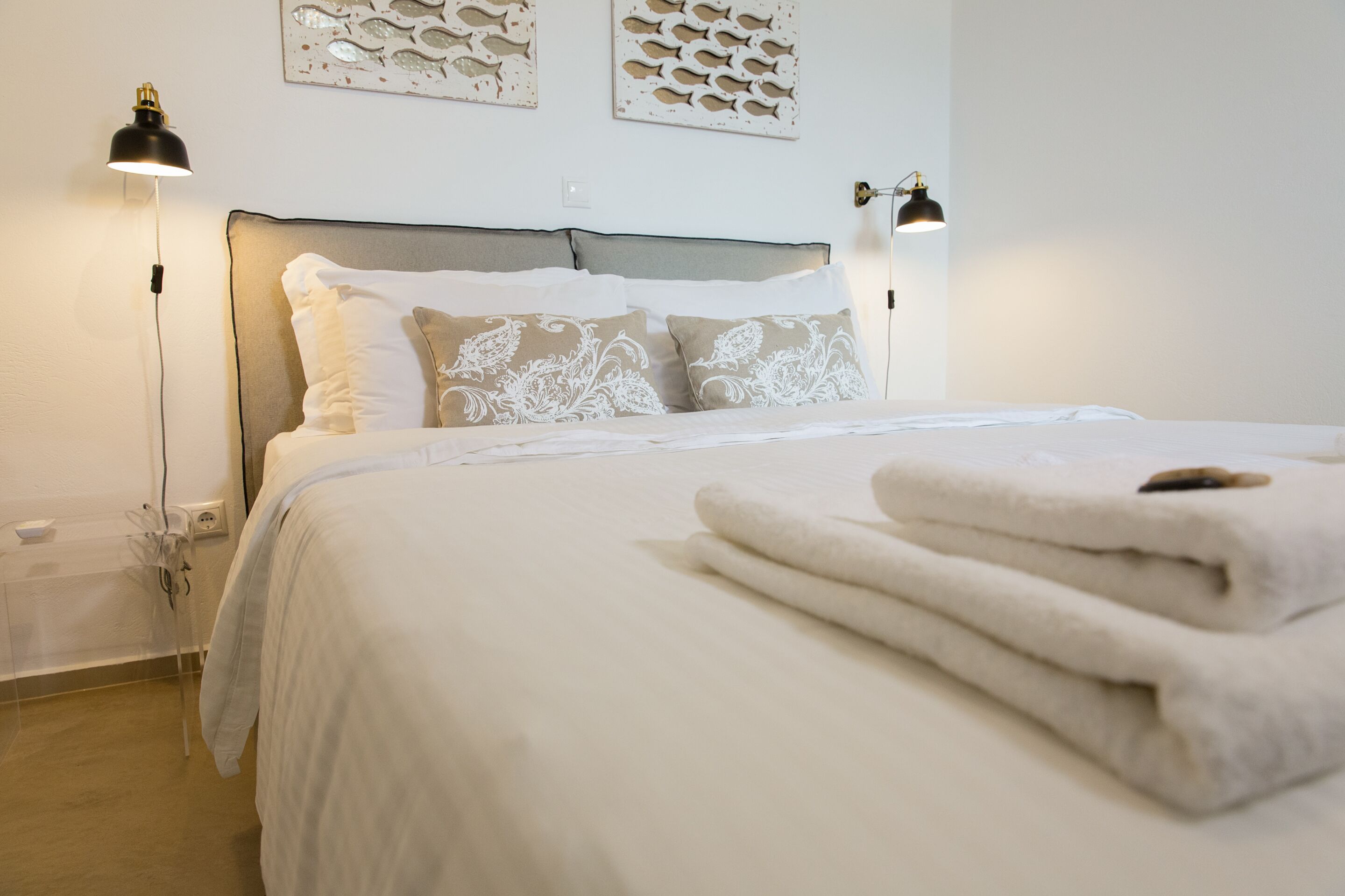 A neatly made bed with white linens and decorative pillows, two bedside lamps, and wall art above the bed.