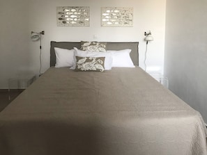 En pænt redt seng med et mønstret sengetæppe og to dekorative puder, en vægmonteret lampe og to billeder på væggen.