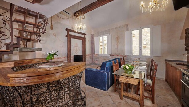 A rustic interior with a wooden bar, blue upholstered seating, a dining table, and a chandelier. - Apartment Leoni Suite in Florence by Mmega (Firenze)